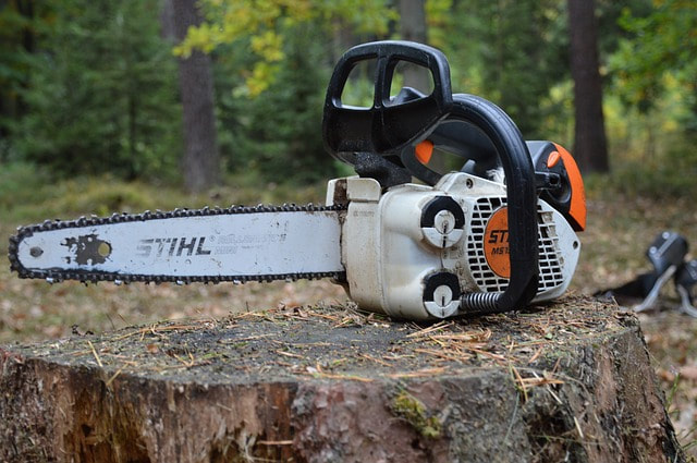 An orange chainsaw resting on top of a tree stump after the tree has been removed